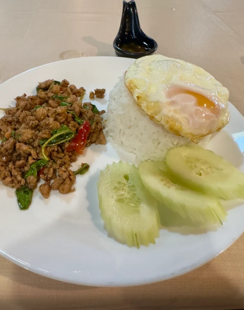 Stir fried minced pork with Basil over rice and fried egg on top on a white plate on a wooden table